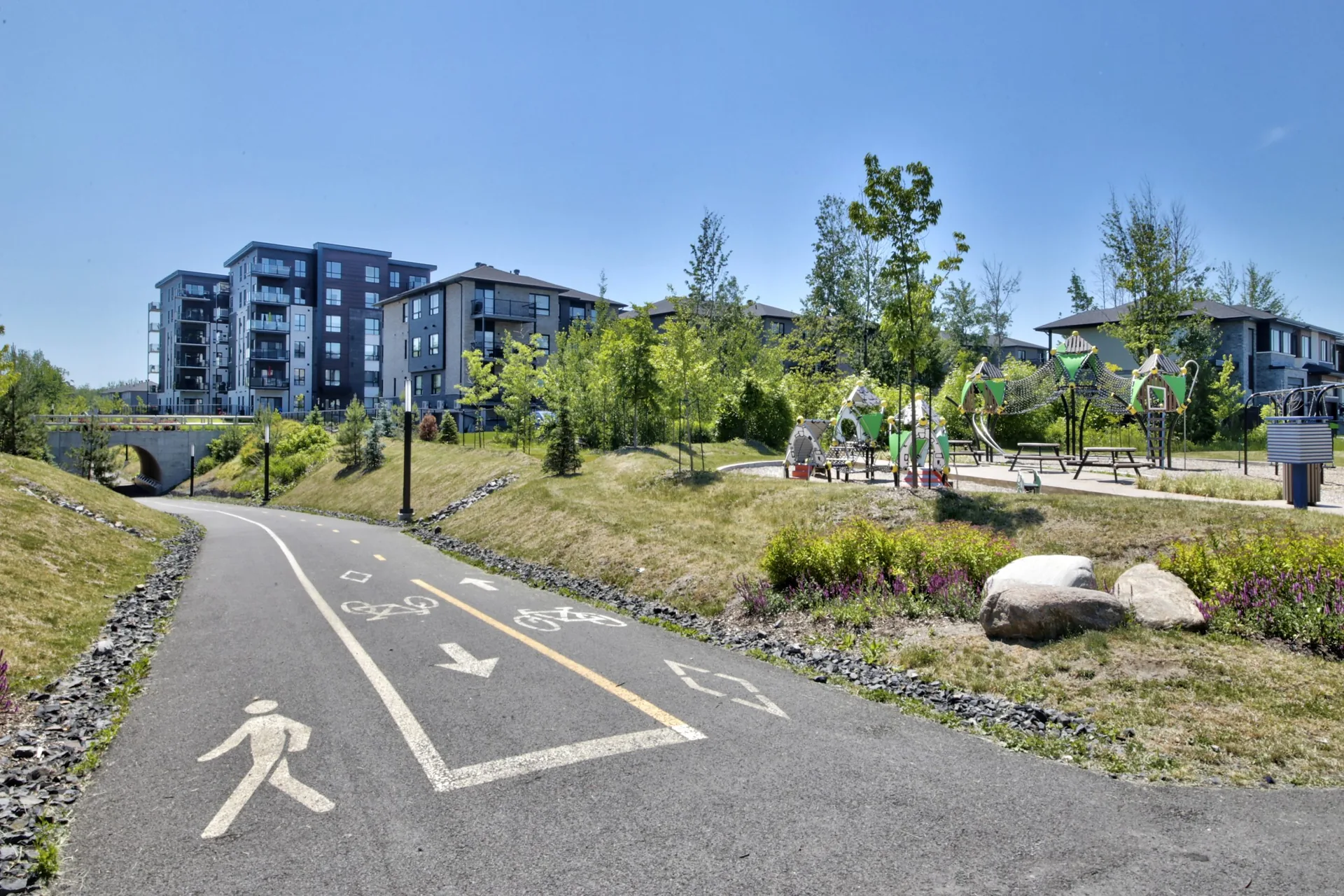 Piste cyclable, aire de jeux et immeubles résidentiels dans Symbiocité à La Prairie.